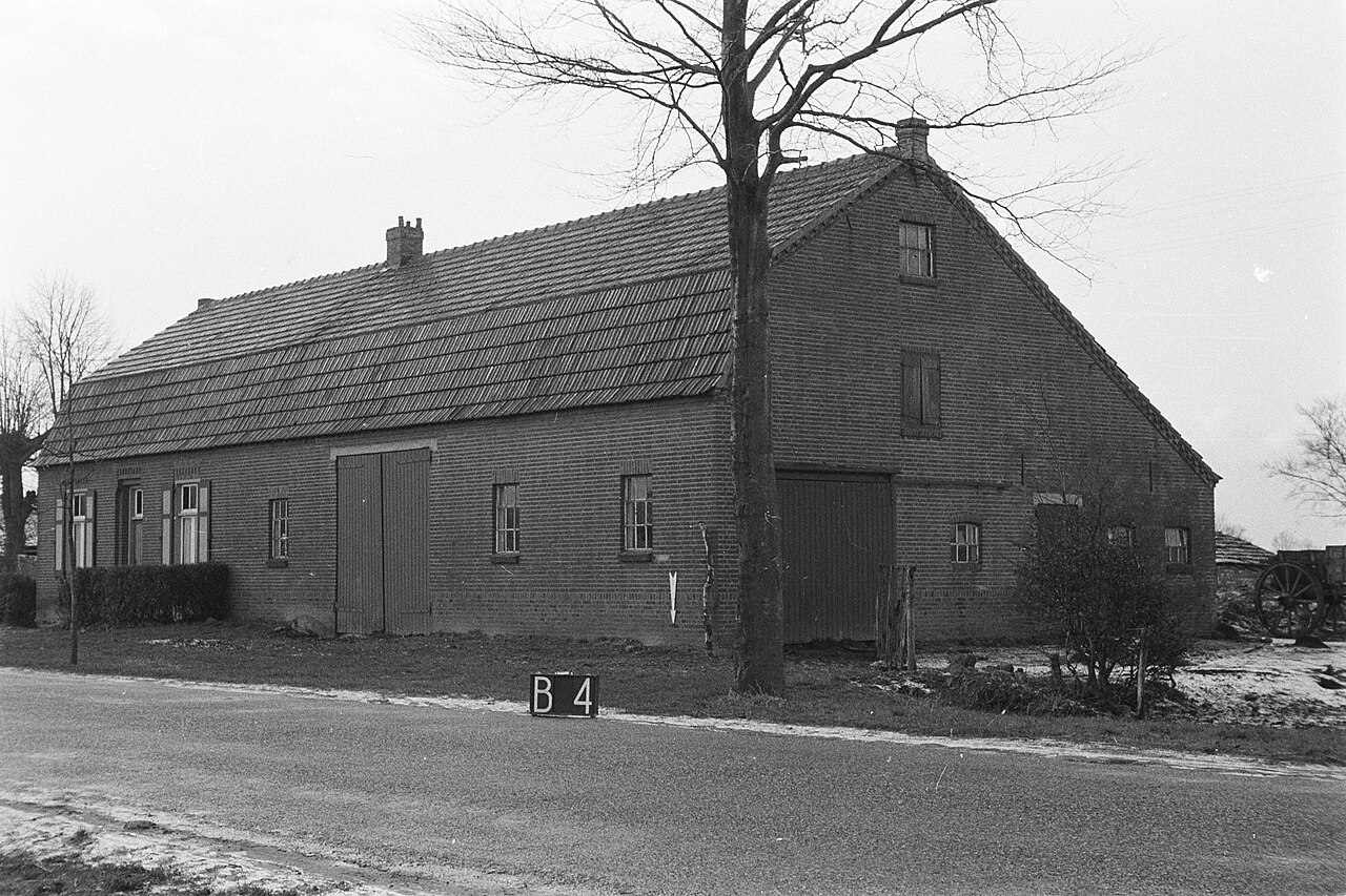 Brede boerderij met twee schuurdeuren en een grote boom aan de weg
